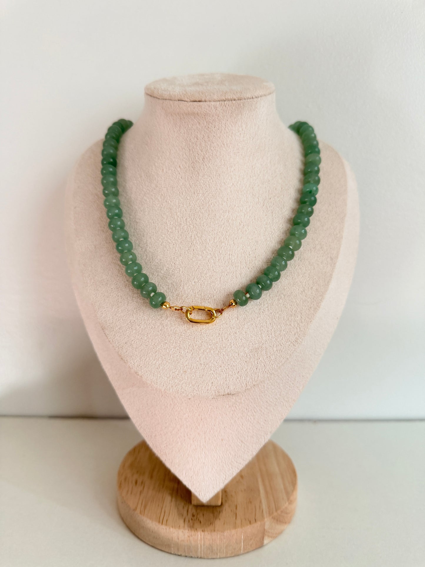 Green beaded bracelet with gold clasp on a beige jewelry display block against a white background