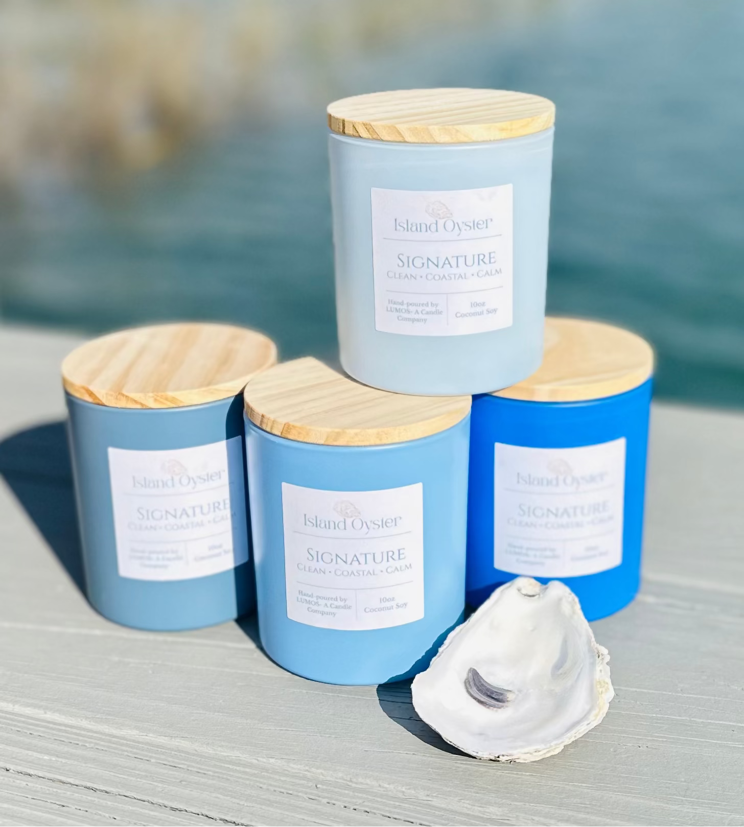 Four candles with wooden lids on a wooden surface near a body of water.