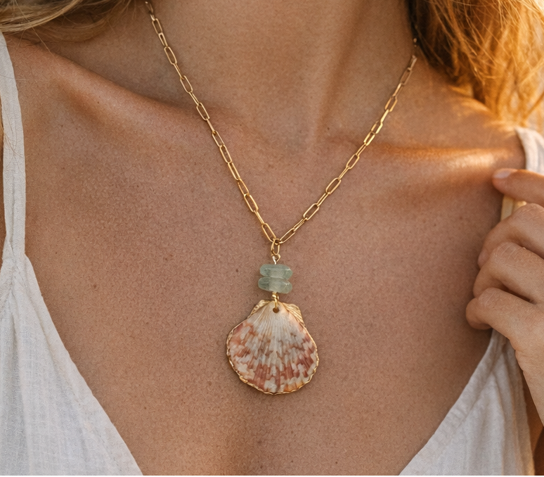 Gold necklace with a shell pendant worn by a person